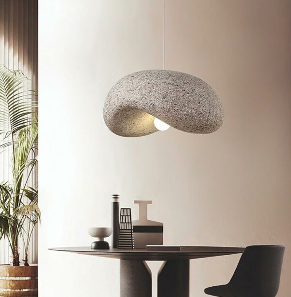Un plafonnier wabi sabi en imitation granit gris suspendu au dessus d'un table dans une maison, une plante sur la gauche de l'image.