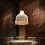 Plafonnier design en osier, suspendu au-dessus d'une table dans un espace sobre, avec une lumière blanche.